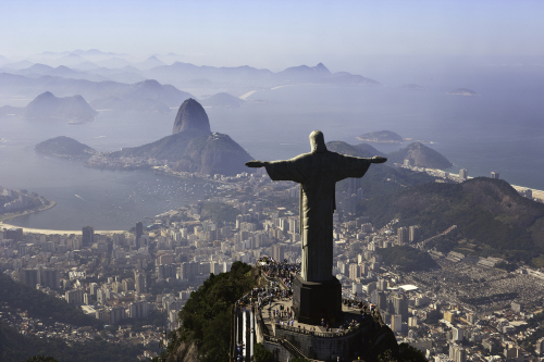 Blick vom Corcovado über die Christusstatue auf Rio de Janeiro, den Zuckerhut und die Meeresbucht unter blauem Himmel.